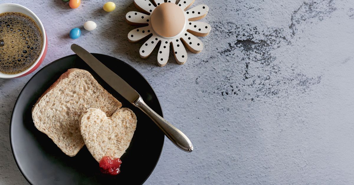 Flat lay of breakfast with coffee, heart-shaped bread, and colorful candies.